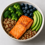 Gehirn-Booster Bowl mit gegrilltem Lachsfilet, Quinoa, frischem Brokkoli, Blaubeeren und Avocadoscheiben in einer weißen Keramikschüssel