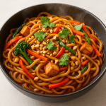 Erdnuss-Nudel-Pfanne in Schüssel: glänzende Nudeln in Erdnusssauce mit Tofu-Würfeln, bunten Gemüsestreifen, gehackten Erdnüssen und frischem Koriander